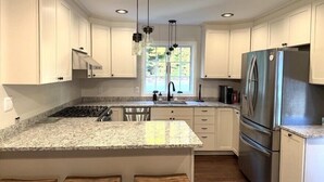 A kitchen with white cabinets, a granite countertop, stainless steel appliances, and wooden stools. - Lakeside Bliss at Pickerel Cove (Laconia)