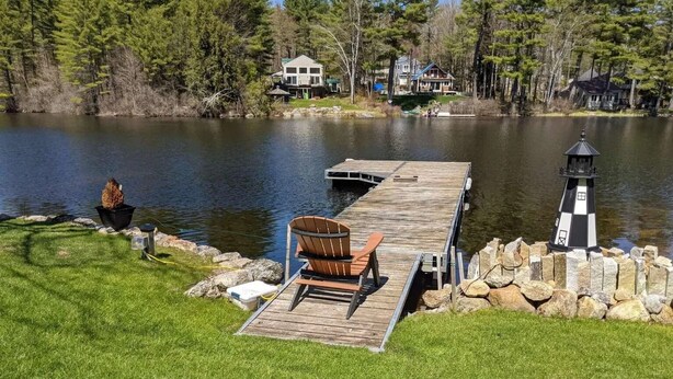 A lakeside deck with a chair, a small dock, and a lighthouse. - Lakeside Bliss at Pickerel Cove (Laconia)