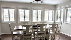 A dining area with a table and six chairs, large windows, and a ceiling fan. - Lakeside Bliss at Pickerel Cove (Laconia)