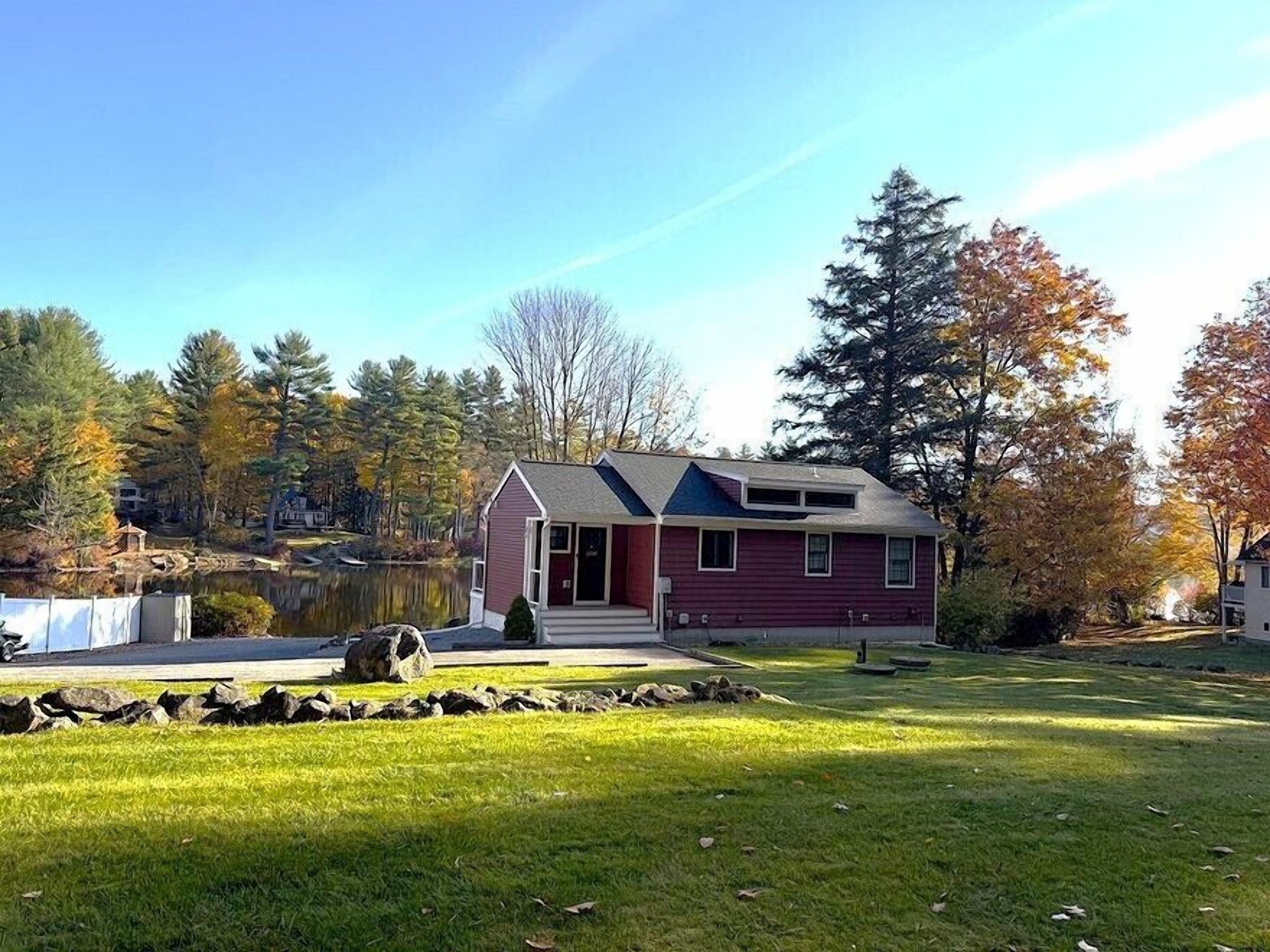 A single-story house with a red exterior and a grey roof, surrounded by a well-maintained lawn and a small pond.