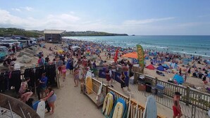 A crowded beach with people, surfboards, and beach umbrellas.