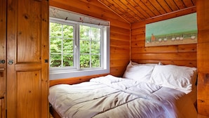 Un dormitorio de cabaña de madera con una cama, una ventana y un cuadro en la pared.