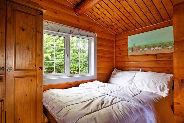 Un dormitorio de cabaña de madera con una cama, una ventana y un cuadro en la pared.