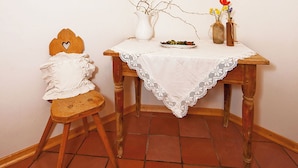 A corner room with a wooden table, a white lace tablecloth, a vase with branches, and a small stool with a heart-shaped decoration. - JAZZ quiet, cozy apartment with sunrise view. 10min from Lake Kaltern (Auer)