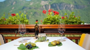 A table set outdoors with two wine glasses, a bottle of wine, a jar of olives, grapes, and a basket of fruit. - JAZZ quiet, cozy apartment with sunrise view. 10min from Lake Kaltern (Auer)