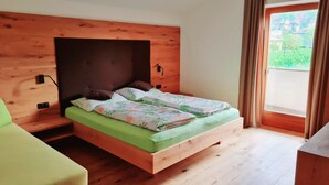 A bed with a wooden headboard, green bedding, and a view of greenery through a window. - JAZZ quiet, cozy apartment with sunrise view. 10min from Lake Kaltern (Auer)