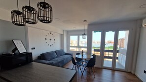 Un espace de vie moderne comprenant un coin cuisine, une table à manger avec des chaises, un canapé et une grande fenêtre donnant sur la ville.