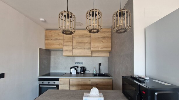 Une cuisine moderne avec des meubles en bois, un îlot central, un micro-ondes noir et trois lampes suspendues.
