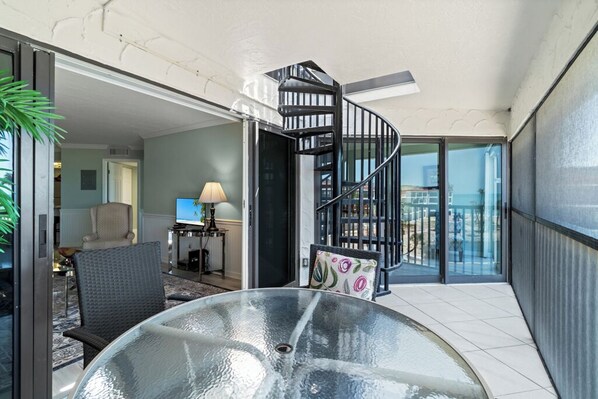 Un intérieur moderne avec une table en verre, un escalier en colimaçon et une vue dégagée à travers des portes vitrées.