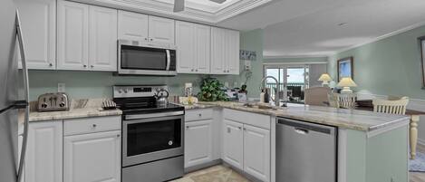 Una cocina moderna con armarios blancos, electrodomésticos de acero inoxidable y un ventilador de techo.