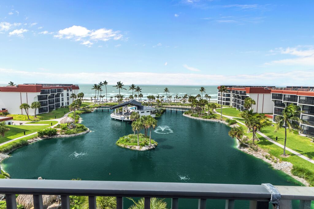 A resort with a central water feature, connected to the ocean, surrounded by palm trees and modern buildings.