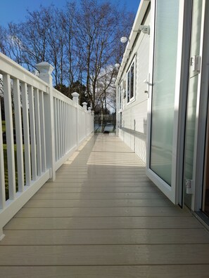 Een houten terras met een witte balustrade, dat leidt naar een gebouw met een glazen deur.