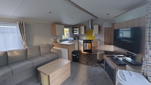 A compact living space with a sofa, a small kitchen area, a dining table, and a television. - 602 Sycamore forest (White Cross)