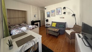 A modern, well-lit room with a bed, sofa, and a desk with a computer. There are wall decorations and a fireplace. - Charming bright studio (La Rochelle)