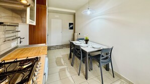 Een kleine keuken met een gasfornuis, houten keukenkastjes en een eethoek met een tafel en stoelen.