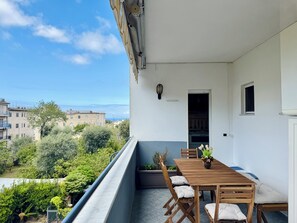 Ein Balkon mit Holztisch und -stühlen, einem Blumentopf und Blick auf Gebäude und Grünflächen.