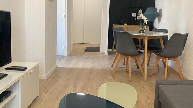 Een moderne woonkamer met een flatscreen televisie, een eettafel met stoelen, een bank en een salontafel.