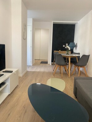 A modern living room with a flat-screen TV, a dining table with chairs, a sofa, and a coffee table. - Cozy Apartment in Strasbourg, Gare, Zénith (Strasbourg)