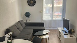 Een moderne woonkamer met een grijze bank, een ronde eettafel met stoelen, een klein bijzettafeltje met een wereldbol, en een plafondlamp.