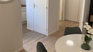 Een moderne, minimalistisch ingerichte kamer met een witte deur, een ronde tafel met een vaas witte bloemen en een zwarte stoel.