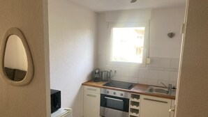 Een compacte keuken met een ingebouwde oven, kookplaat, spoelbak en een raam voor natuurlijk licht.