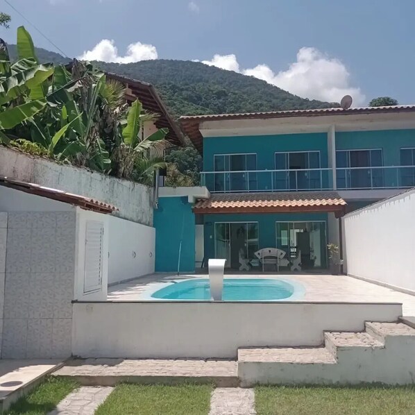 A two-story house with a swimming pool, a covered patio, and a mountain in the background.