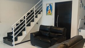 A living room with a black leather sofa, a black couch, a staircase with white railings, and a ceiling fan.