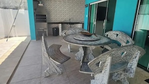 A dining area with a round table and four chairs, a kitchen in the background, and a sliding glass door leading to an outdoor area.