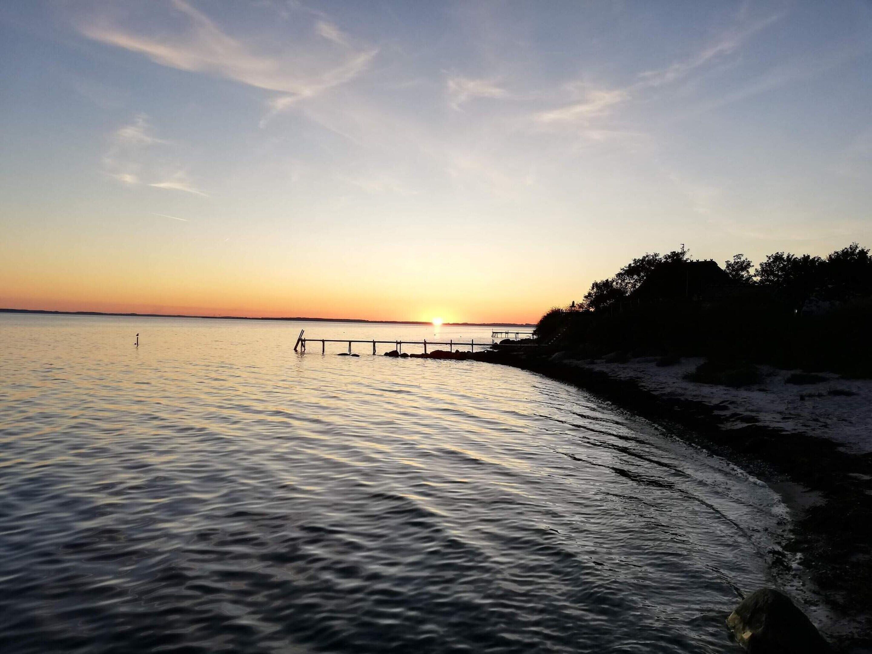 Um pôr do sol sobre águas calmas, com um cais que se estende na água.