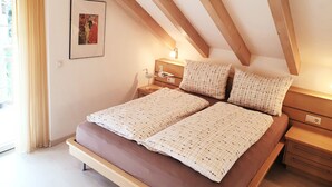 A bedroom with a sloped ceiling, a bed with patterned bedding, a bedside table with a lamp, and a framed picture on the wall. - PINK LADY family-friendly vacation home, 10 minutes from Lake Kaltern (Auer)