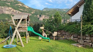 A wooden play structure with a slide, a trampoline, and a stone wall. - PINK LADY family-friendly vacation home, 10 minutes from Lake Kaltern (Auer)