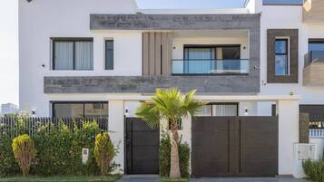 Une maison moderne à deux étages, dotée d’un toit plat, de grandes fenêtres et d’une entrée sécurisée par un portail.