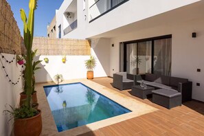 A modern outdoor pool area with a built-in seating area and potted plants.