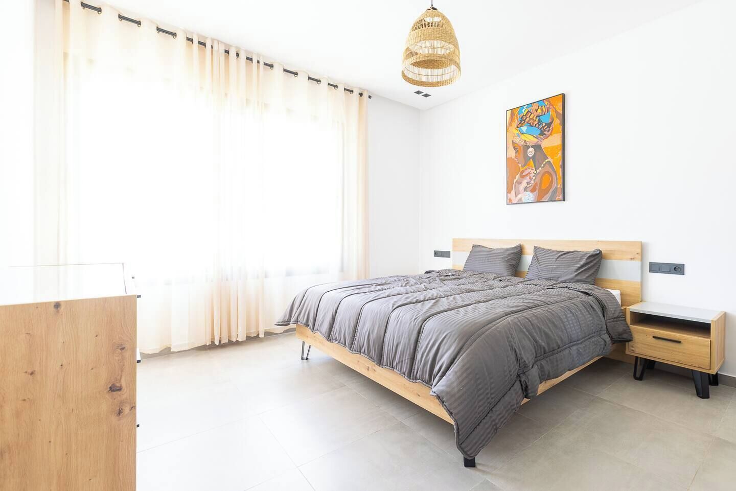 Ein modernes Schlafzimmer mit einem hölzernen Bett, einem Nachttisch, einer Lampe und einem Bild an der Wand.