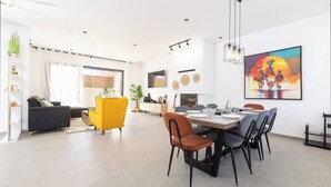 Una sala moderna con un sofá, un sillón amarillo y un comedor con una mesa dispuesta para seis personas.