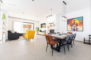 A modern living room with a sofa, a yellow armchair, and a dining area with a table set for six.