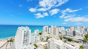 A coastal cityscape with high-rise buildings, a beach, and a clear blue sky. - Deluxe Ocean View Studio with Free Parking & Pool (San Juan)