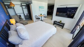 A hotel room with a large bed, a desk with a chair, a small table with two chairs, a TV mounted on the wall, and a blue wall with a picture frame. - Deluxe Ocean View Studio with Free Parking & Pool (San Juan)