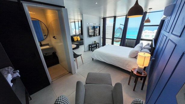 A modern hotel room with a large bed, a desk, a chair, and a view of the ocean. - Deluxe Ocean View Studio with Free Parking & Pool (San Juan)