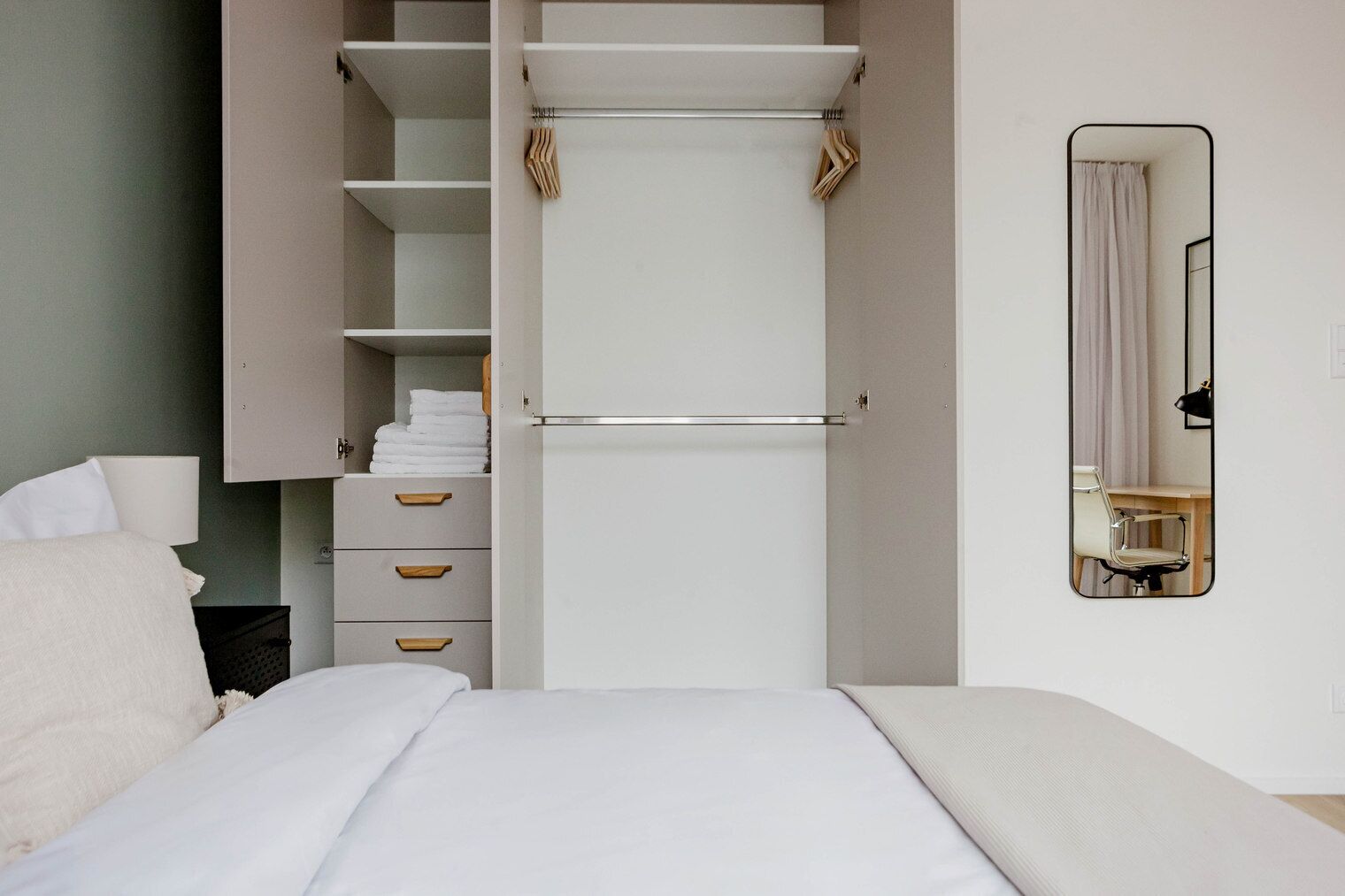 Un dormitorio con cama, armario con espacio para colgar, escritorio con silla y espejo en la pared.