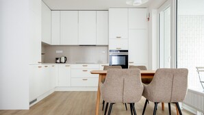 Une cuisine moderne avec des meubles blancs, un four noir et une table à manger avec deux chaises.