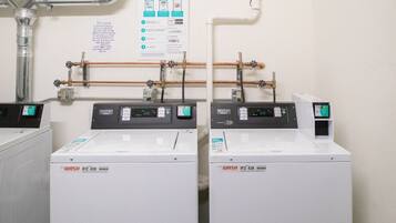 Twee Maytag wasmachines in een wasruimte met zichtbare leidingen en een bedieningspaneel.