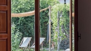 A room with a dining table, chairs, and a view of a garden with a hammock and two lounge chairs.