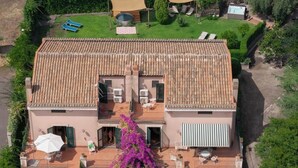 Una casa de dos pisos con techo de tejas, un balcón y un patio con mobiliario exterior.