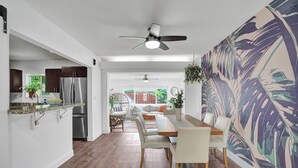 Uma cozinha moderna com frigorífico embutido, sala de jantar com mesa e cadeiras de madeira e um grande mural na parede.