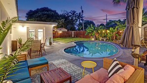 Um quintal com piscina, móveis de jardim e cerca de madeira.