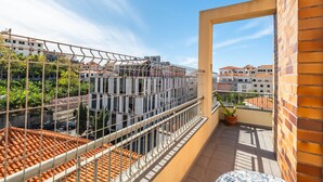 A balcony with a metal railing, a potted plant, and a view of a cityscape with buildings and a clear sky.