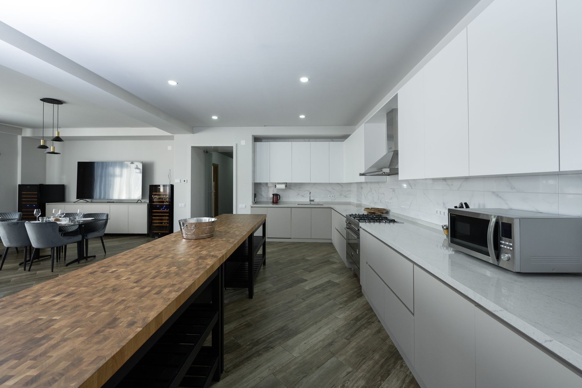A modern kitchen with white cabinets, a wooden dining table, and a built-in microwave.