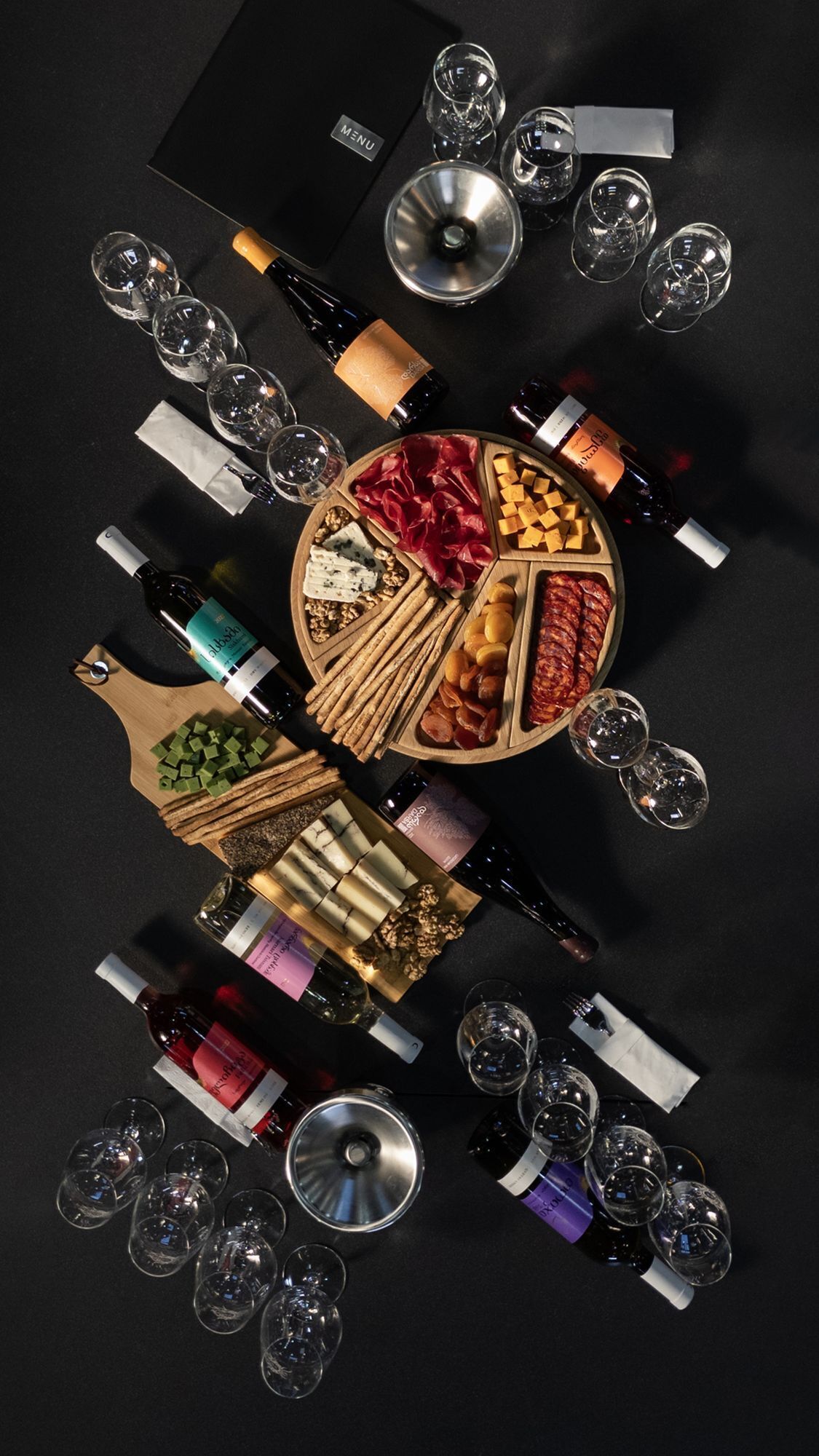 Une table dressée avec divers plats et des bouteilles de vin, entourée de verres à vin vides.