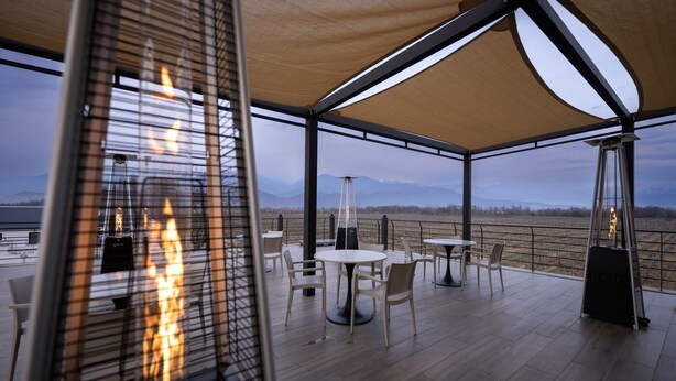 Een terras buiten met tafels en stoelen, een vuurplaats en uitzicht op het landschap.